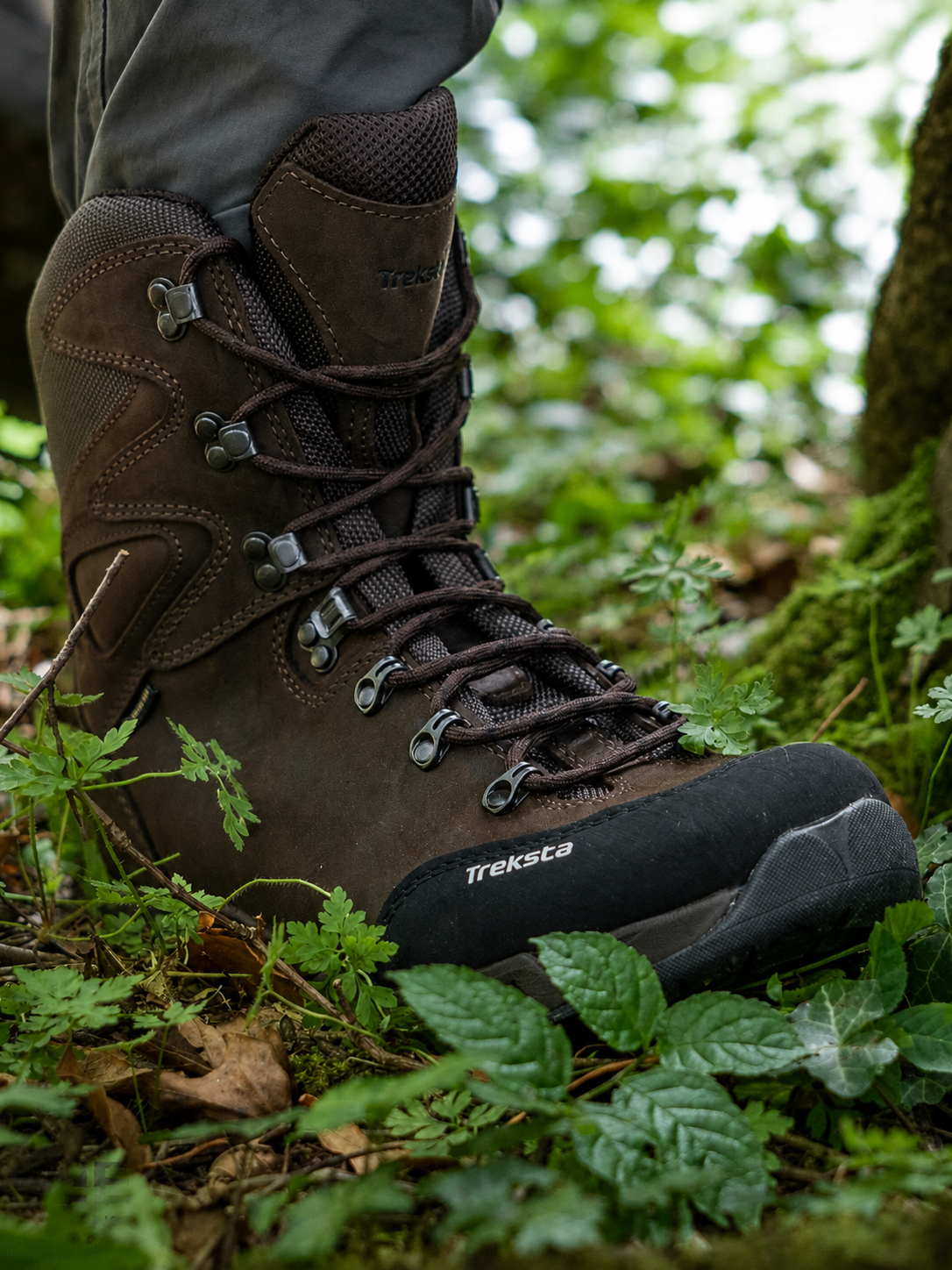 Brown hiking boot with visible brand name on a forest floor