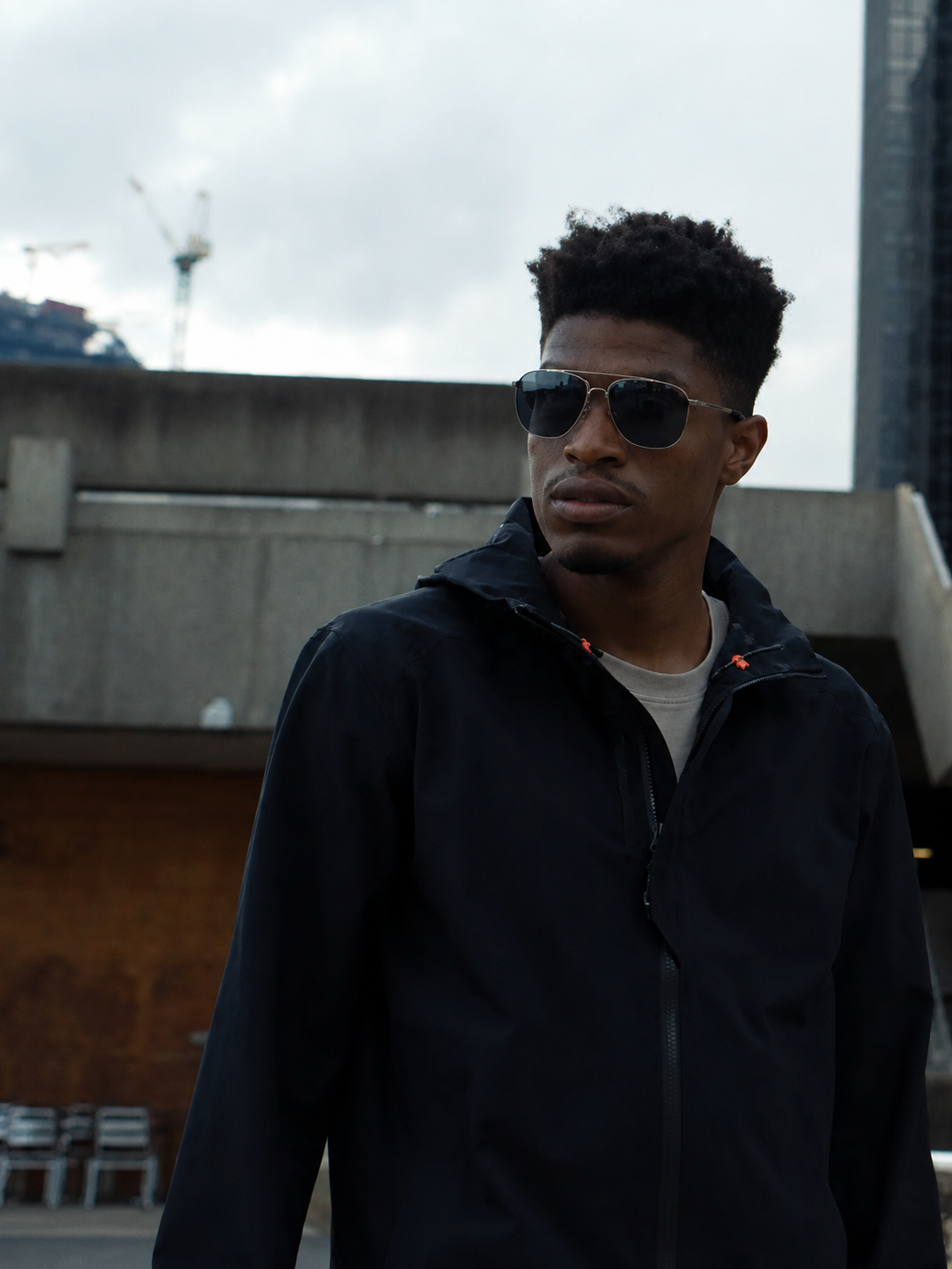 Man wearing Bolle sunglasses and a dark jacket outdoors with a cityscape background