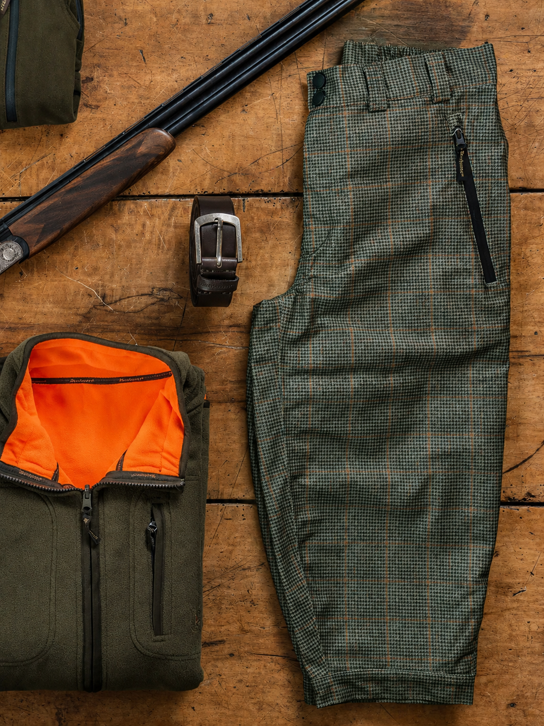 Green hunting breeks and bag on a wooden surface with a rifle and belt.