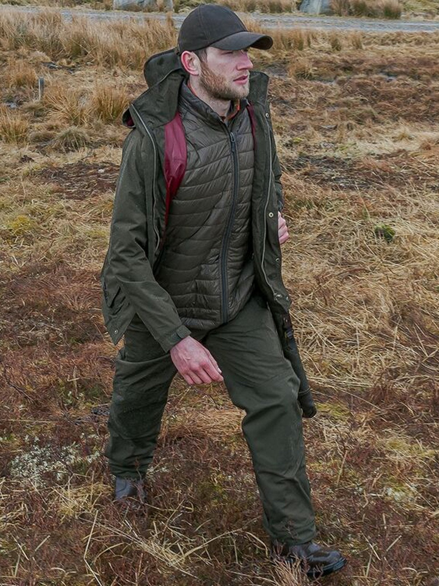 Man in green jacket and pants standing in a dry, open field.