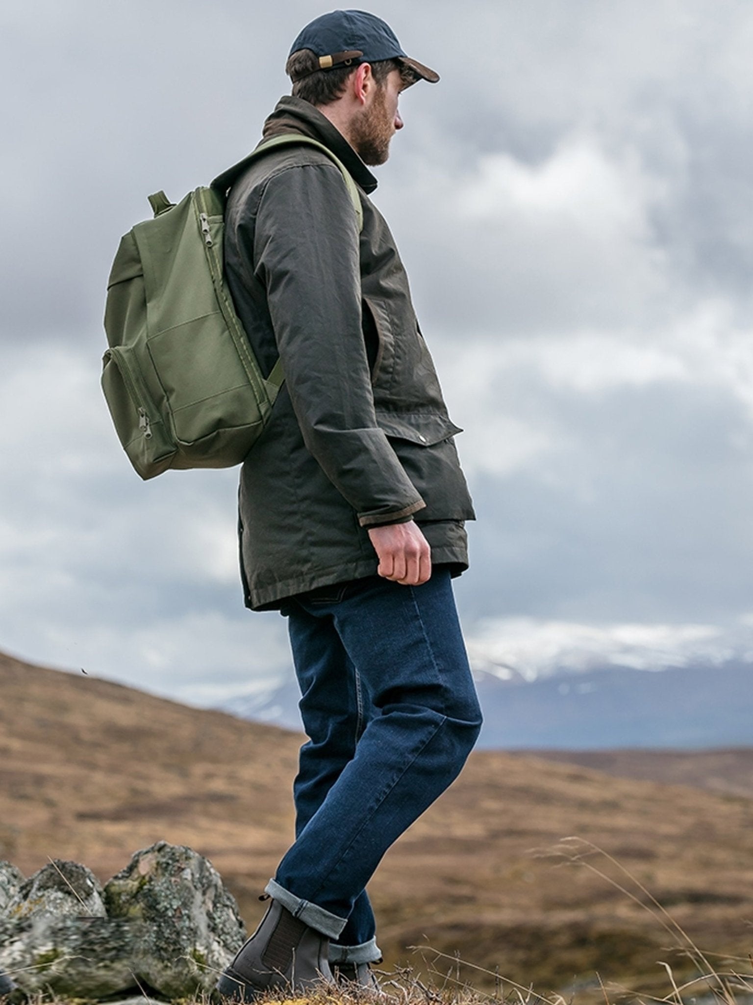 Man with a green backpack walking in a mountainous landscape