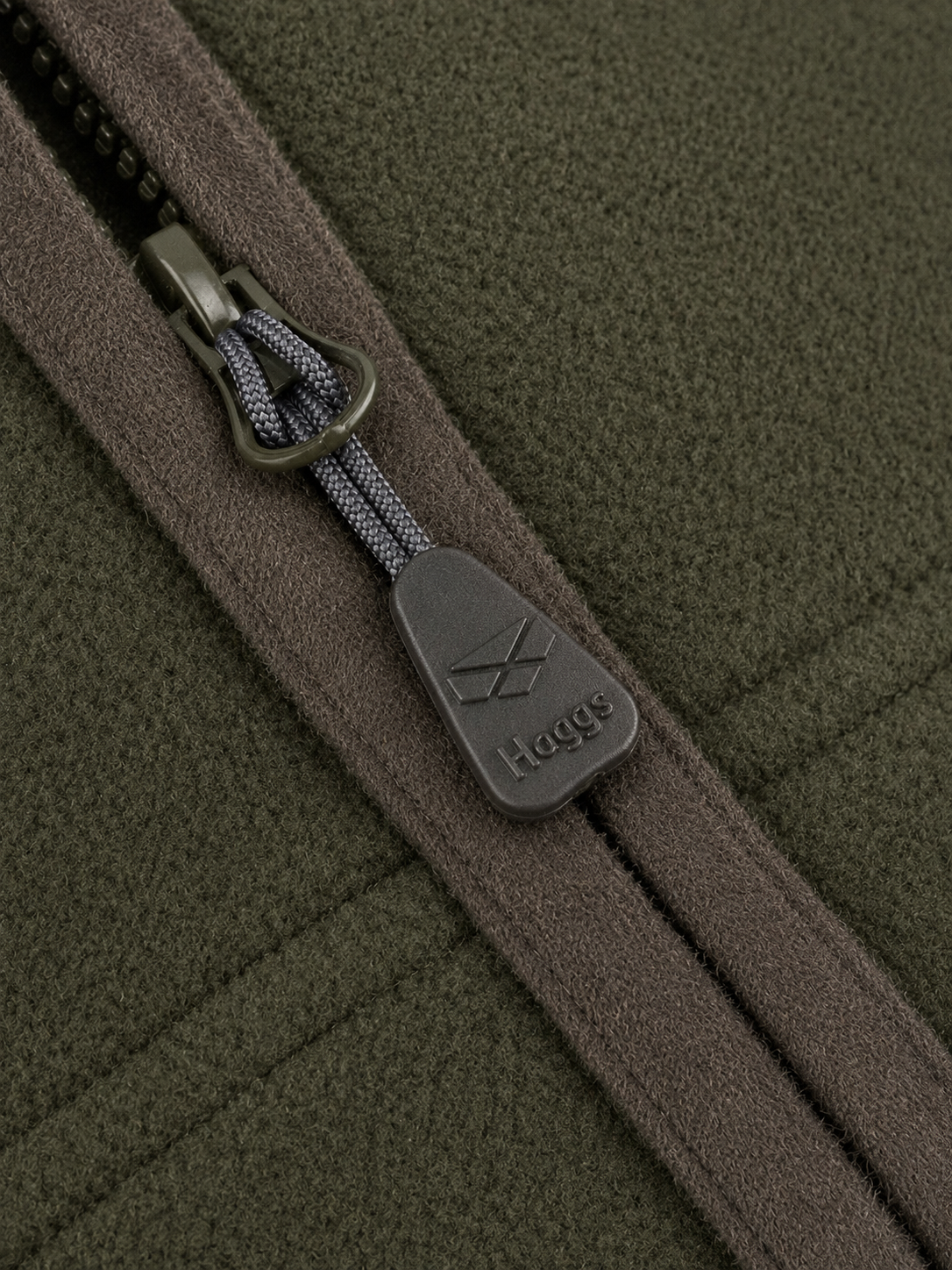 Close-up of a zipper on a green fabric with a brand logo.