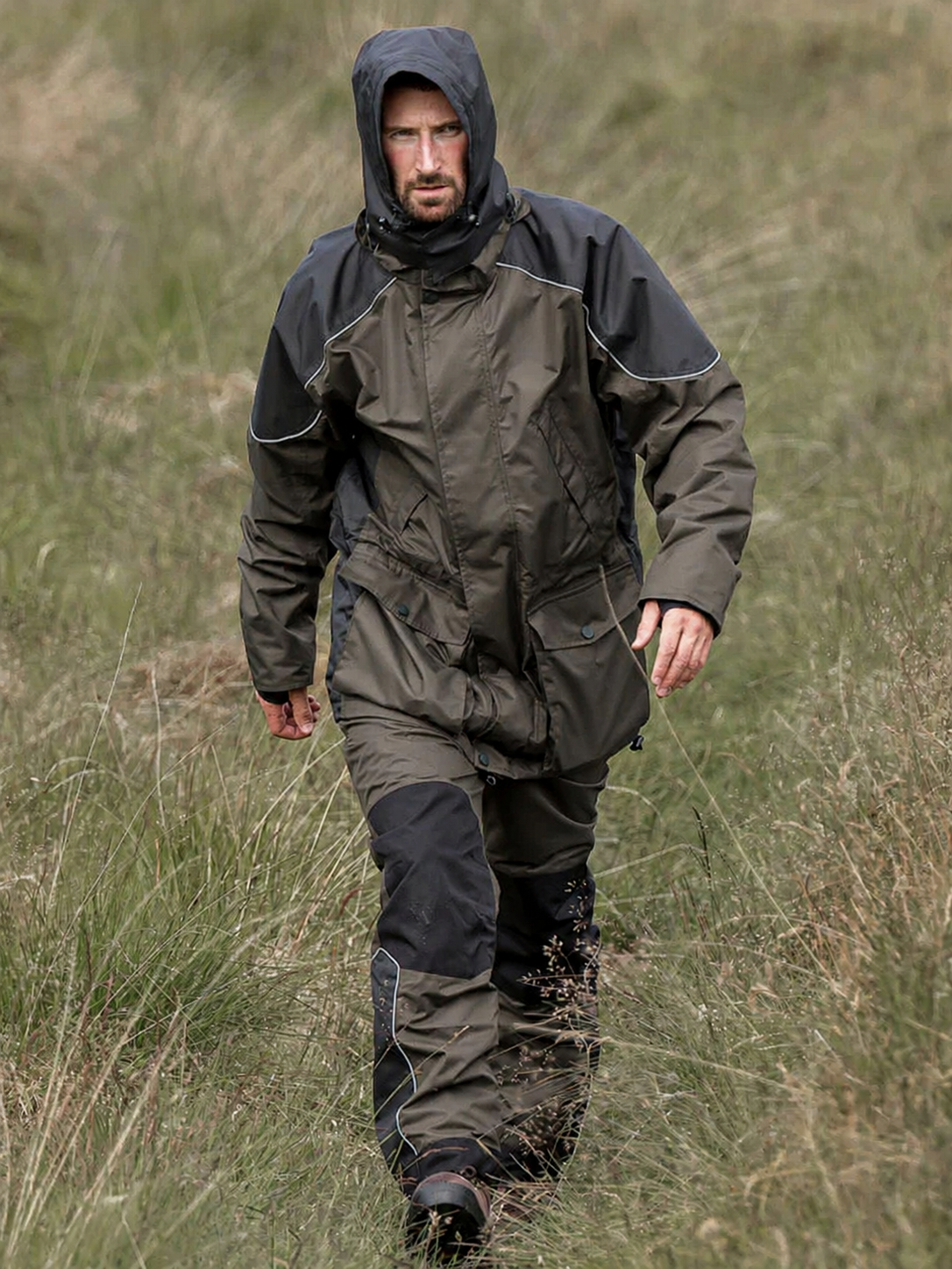 Man wearing a raincoat walking through a grassy field