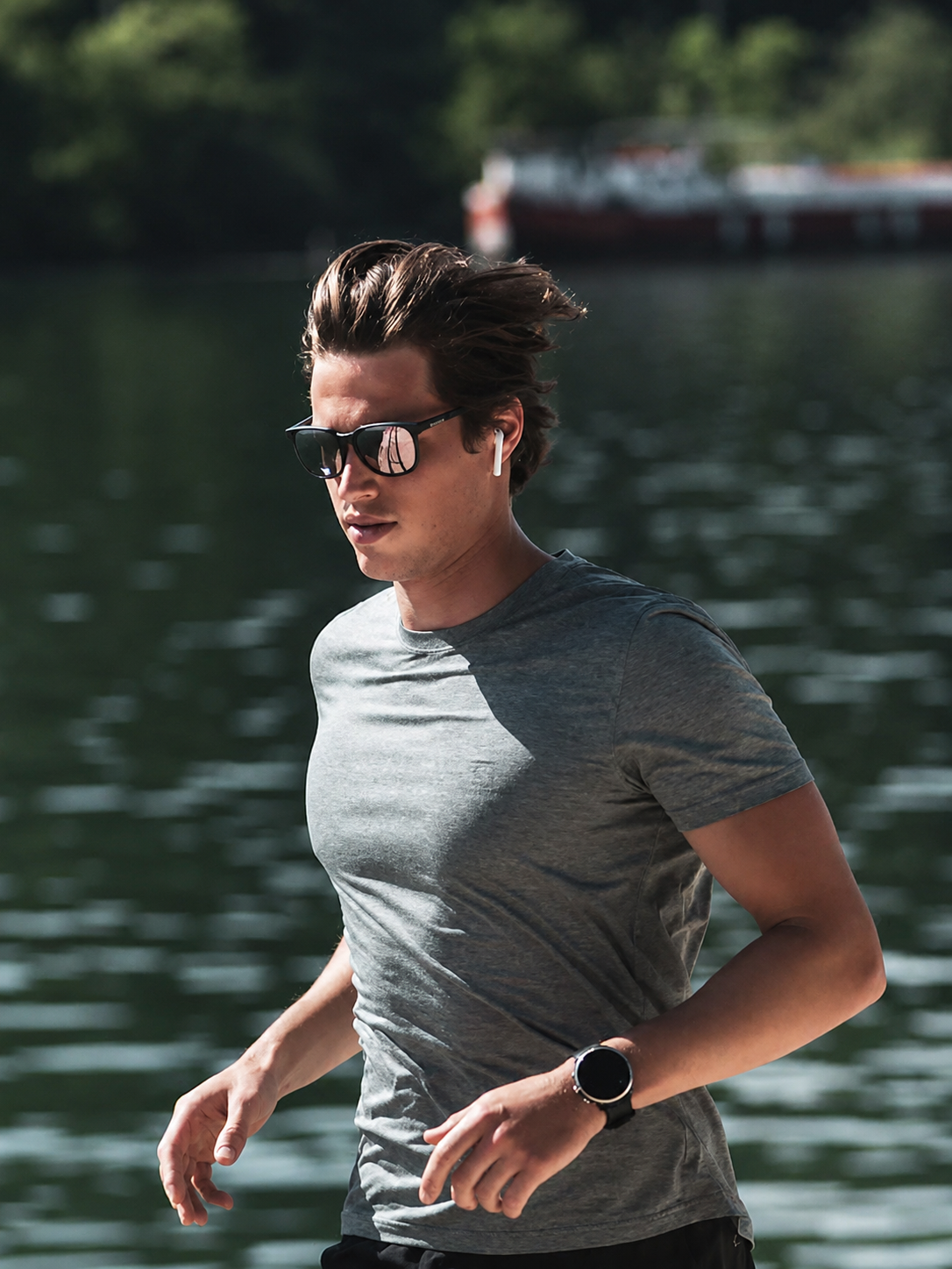 Man wearing Bolle sunglasses and a gray t-shirt by a body of water