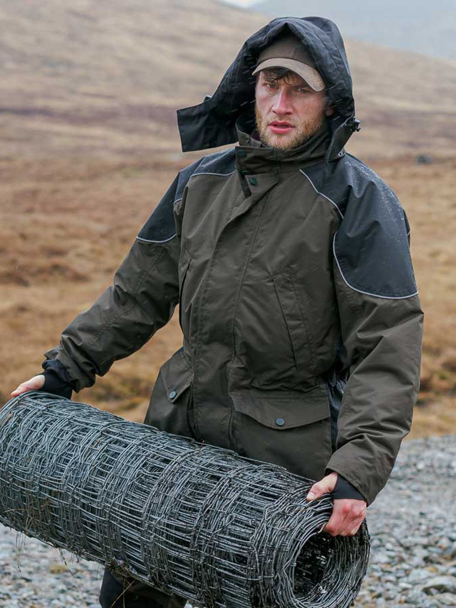 Man in a dark jacket holding a roll of wire mesh in a rural setting