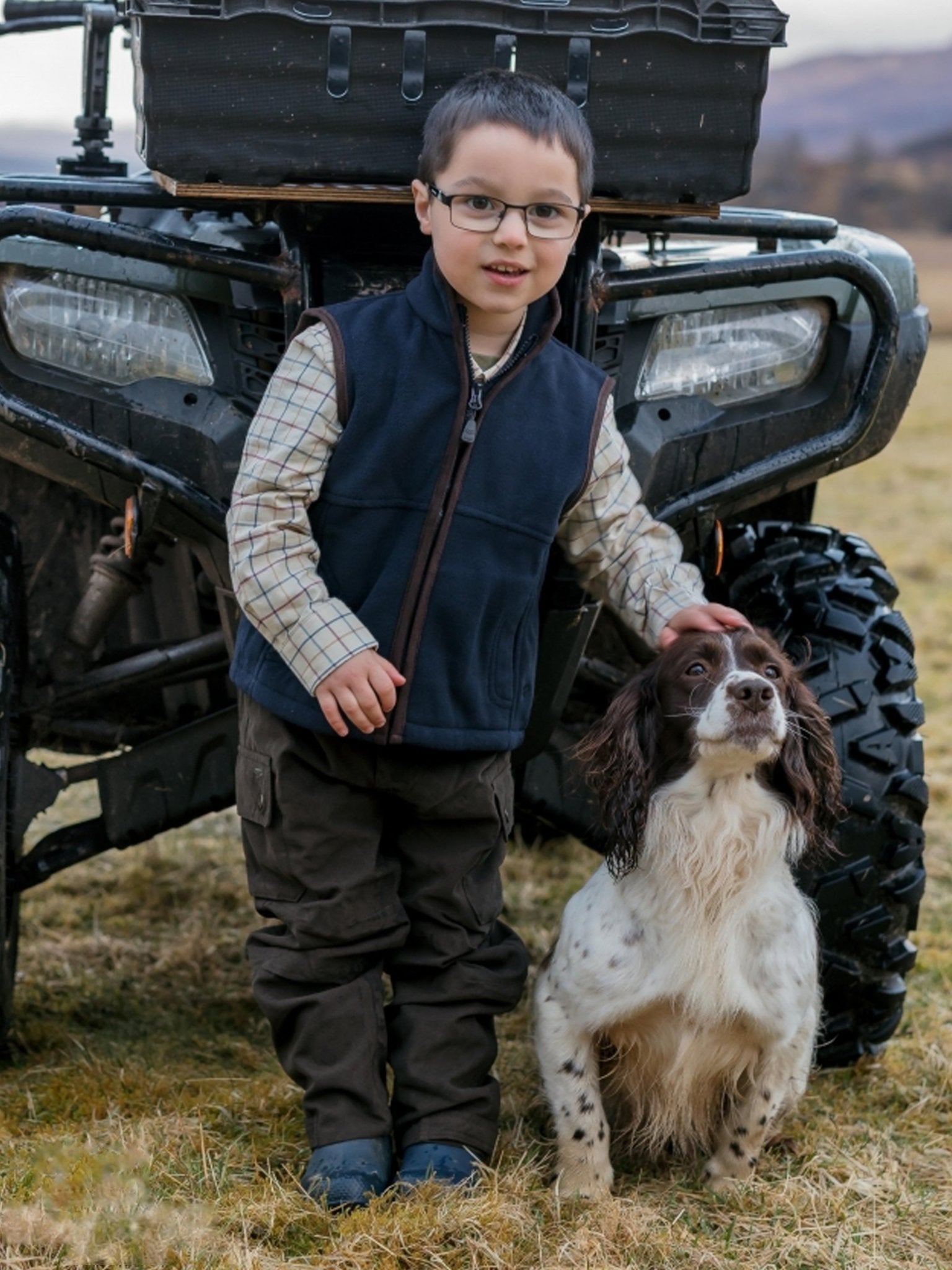 Child with glasses and a dog standing next to an ATV in a field