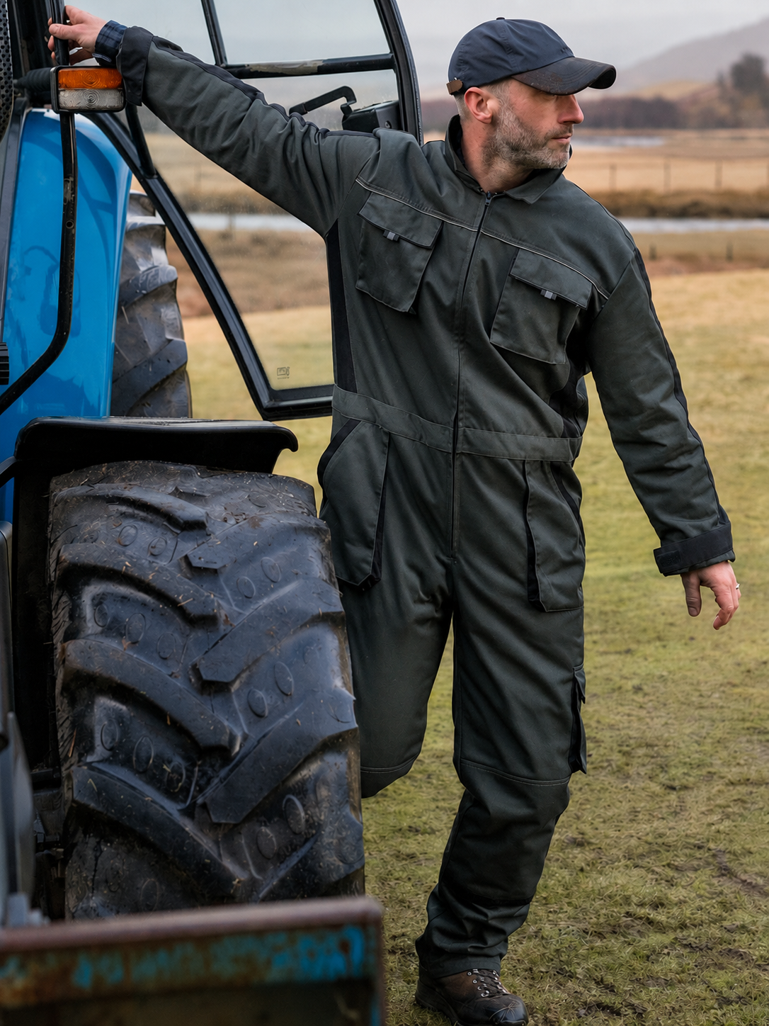 Man in green Hoggs of Fife overall standing next to a blue tractor in an outdoor setting