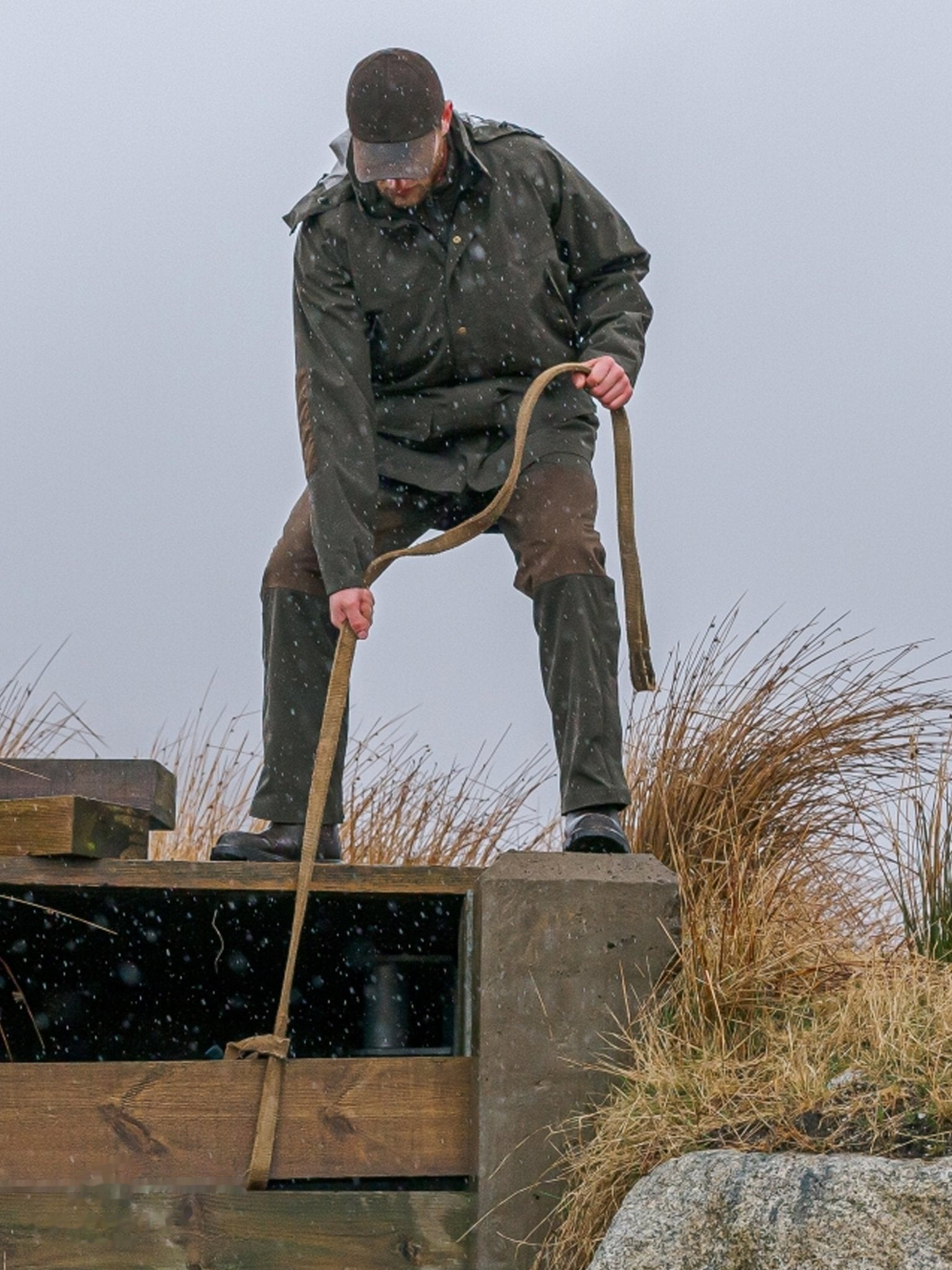 Person in outdoor setting pulling a long strap, standing on a concrete platform with grass and rocks in the background.