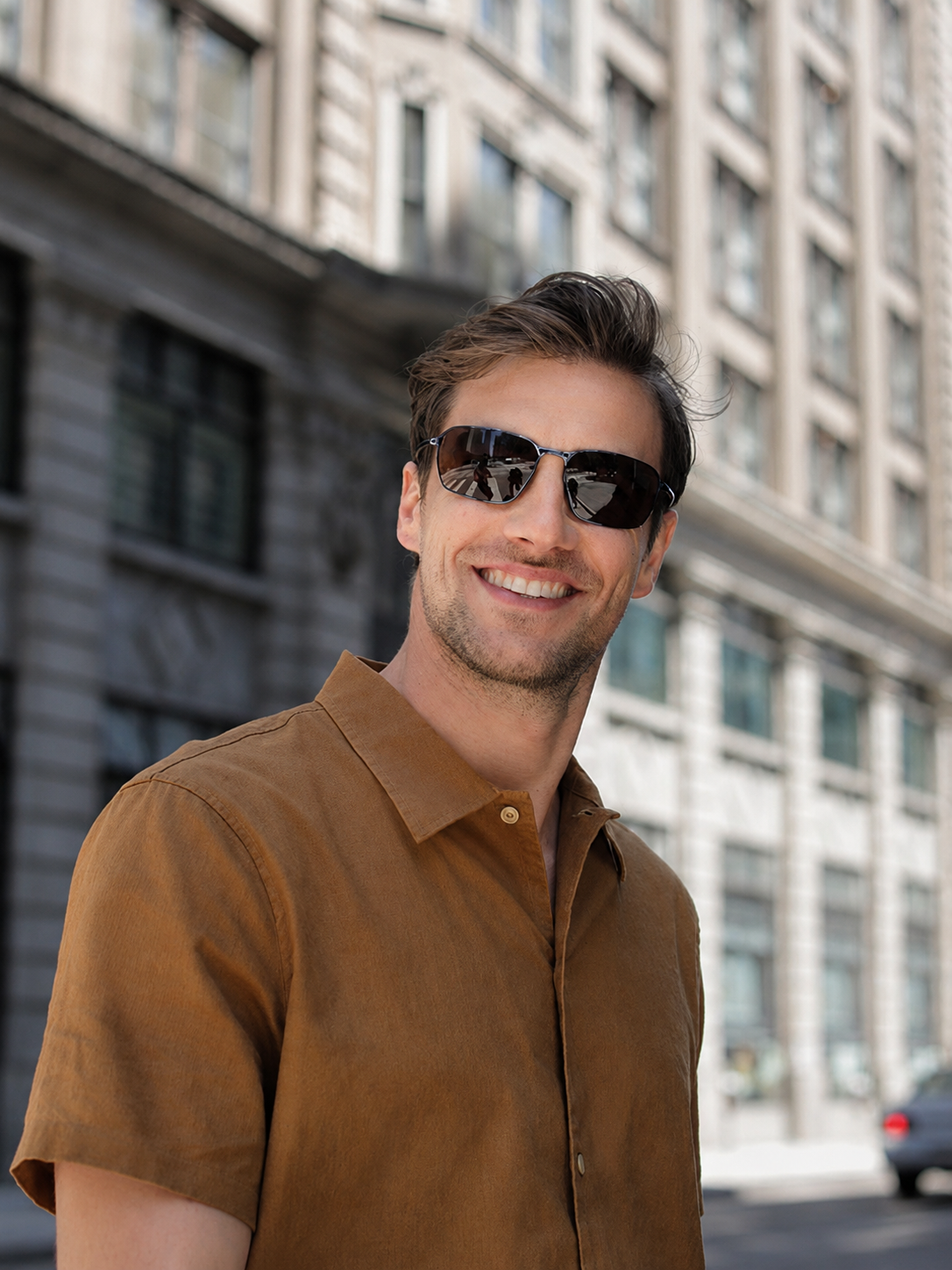 Man wearing Serengeti sunglasses and a brown shirt standing in an urban setting