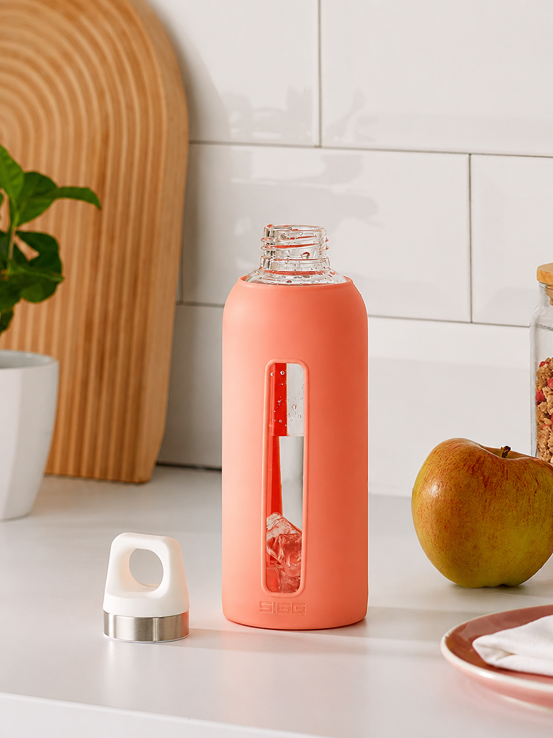 Coral-colored water bottle with a clear window on a kitchen counter.
