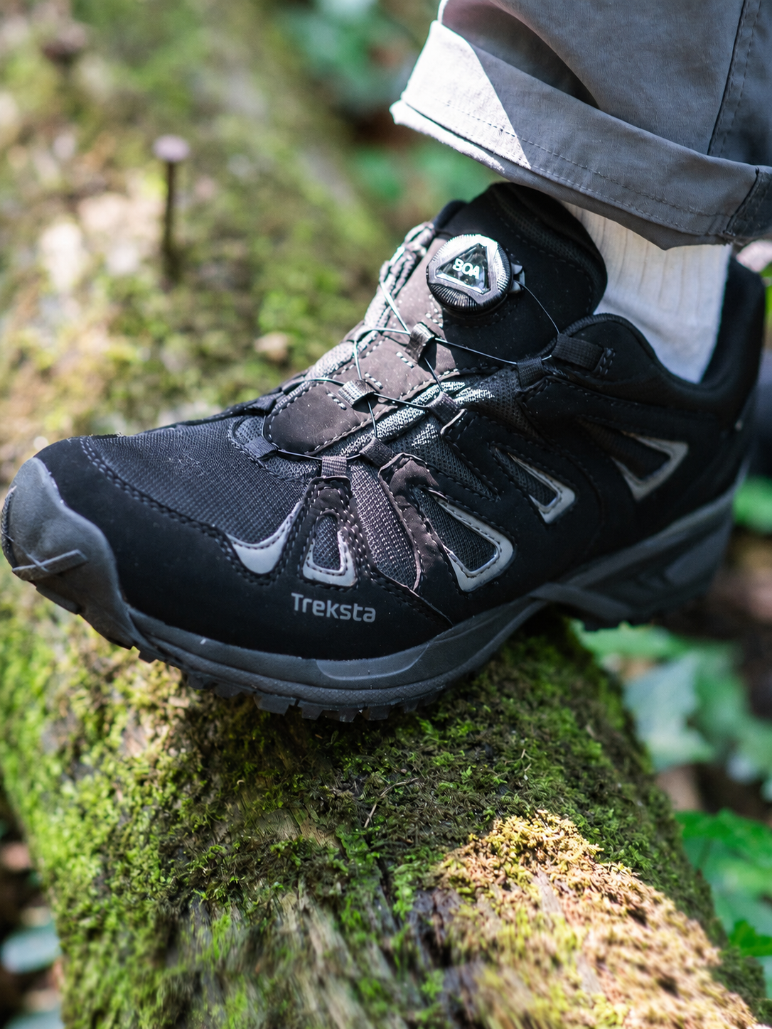 Black hiking shoe with visible brand name on a mossy tree trunk